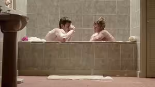 A young man and woman sit facing each other in a bathtub