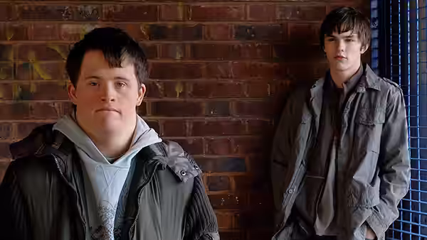 Ben Philips (Tommy Jessop) stands before David Philips (Nicholas Hoult) beside a brick wall