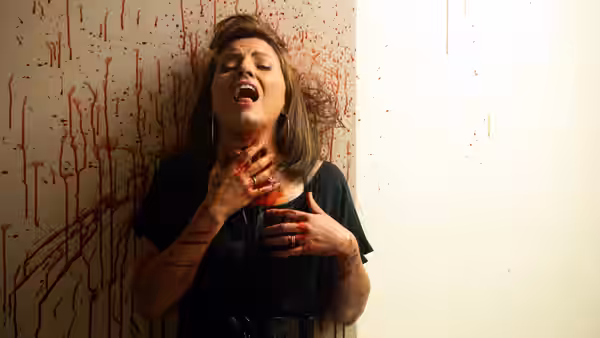 A bloodied woman clutches her throat against a wall splattered with blood