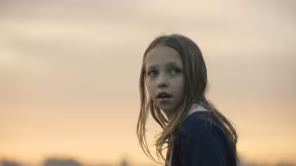 A young girl looks back over her shoulder against a pale evening sky