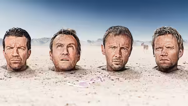 Four men buried up to their necks in desert sand, staring ahead
