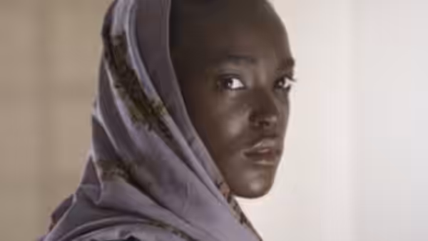 A young woman in a patterned headscarf looks over her shoulder