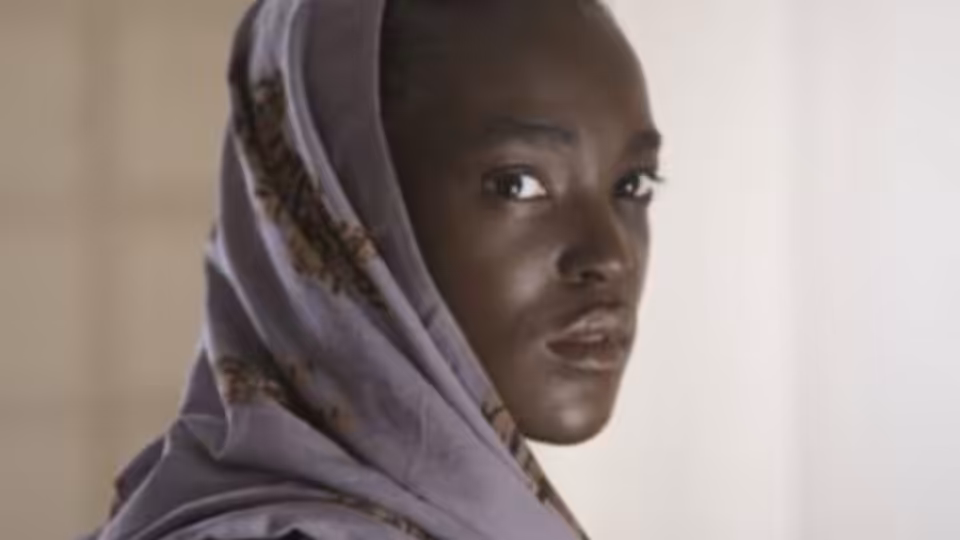 A young woman in a patterned headscarf looks over her shoulder