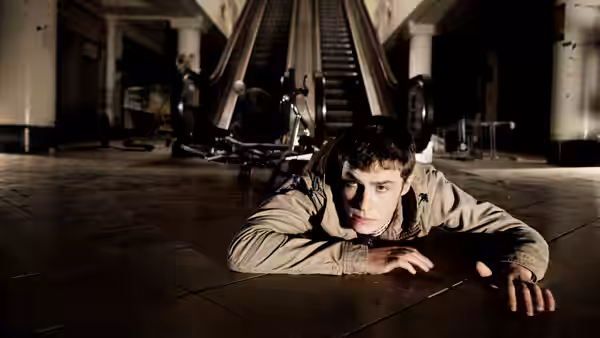 Paul Roberts (Iain De Caestecker) lies on the floor beneath escalators as figures approach