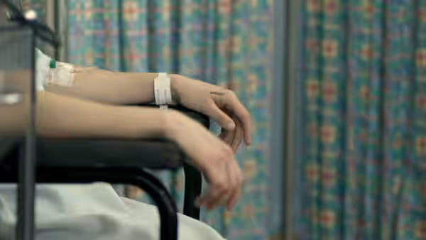 A hospital patient's hands hang over the edge of a bed, wristbands visible