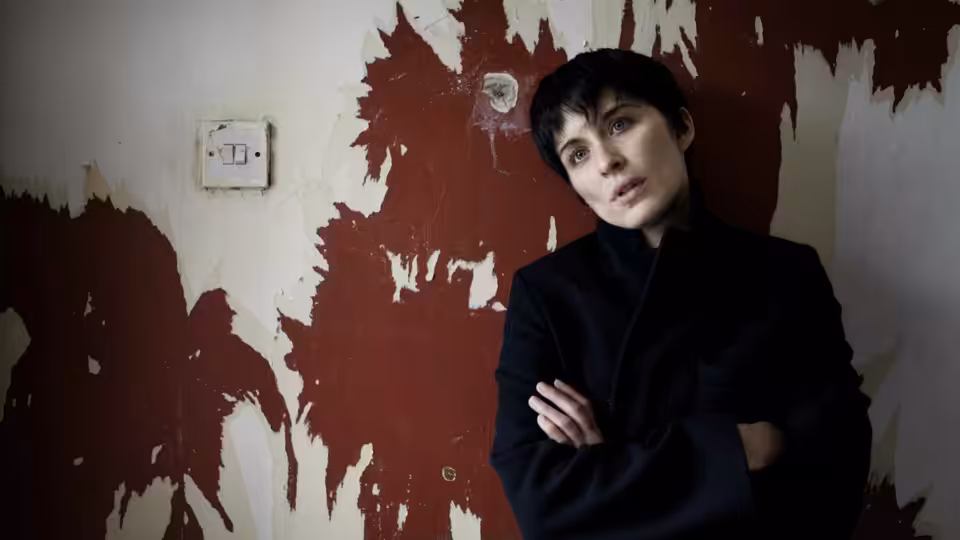 Lol (Vicky McClure) stands with her arms crossed against a peeling wall
