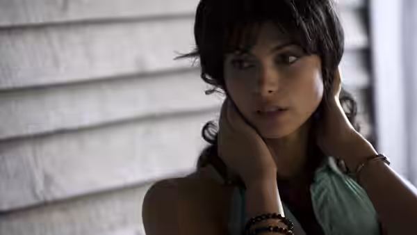 Rose Montgomery (Morena Baccarin) holds her hands behind her neck beside a clapboard wall