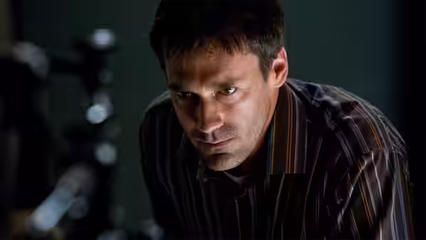 A man leans forward intently in a dimly lit room