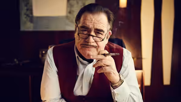 Sydney Newman (Brian Cox) sits at a desk holding a cigar
