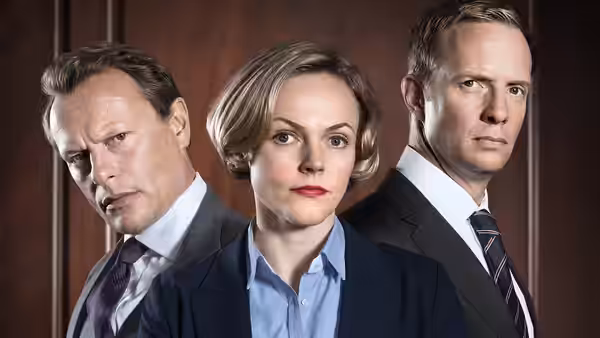 Martha Costello stands between two male barristers against a wood-panelled wall