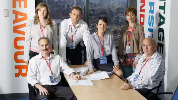Office staff gather around a table covered with papers