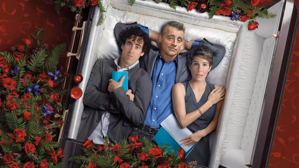 Matt LeBlanc, Sean Lincoln (Stephen Mangan) and Beverly Lincoln (Tamsin Greig) lie together in a flower-lined coffin