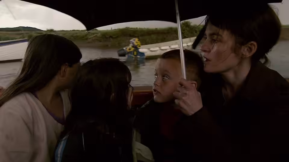 A woman and three children ride beneath a boat canopy, watching a person in the water