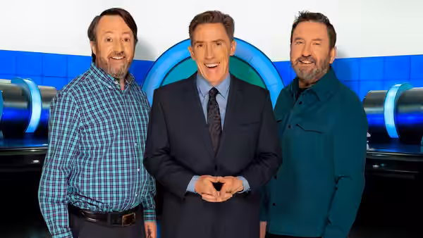 Lee Mack, Rob Brydon and David Mitchell stand together on the studio set