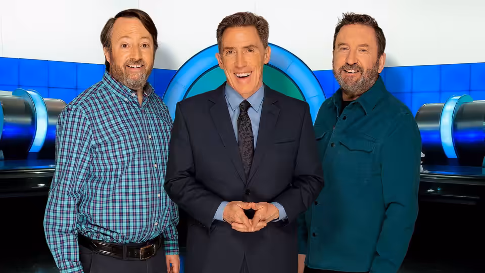 Lee Mack, Rob Brydon and David Mitchell stand together on the studio set