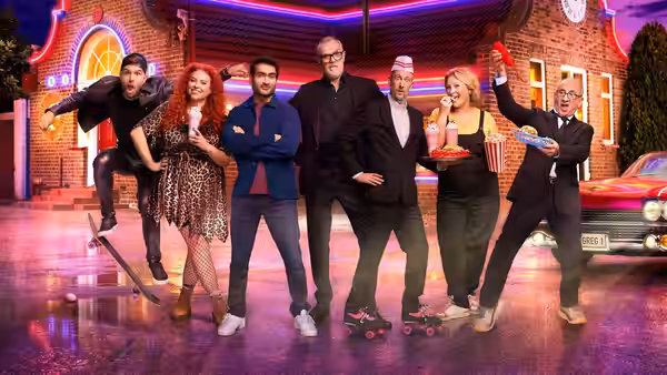 Greg Davies and a group of comedians pose outside a brightly lit diner