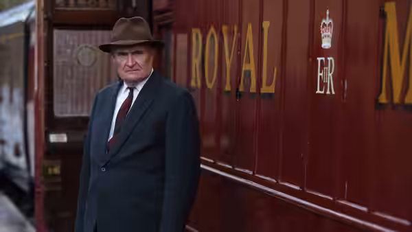 An older man in a fedora stands beside a Royal Mail train