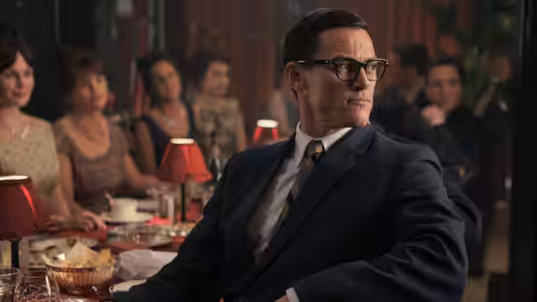 A bespectacled man turns in his chair at a crowded dining table