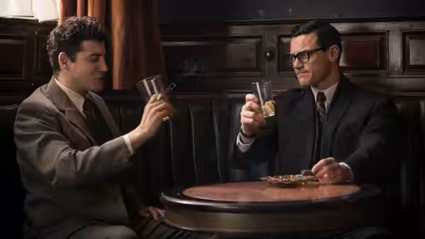 Two men raise their glasses across a small table in a wood-paneled pub