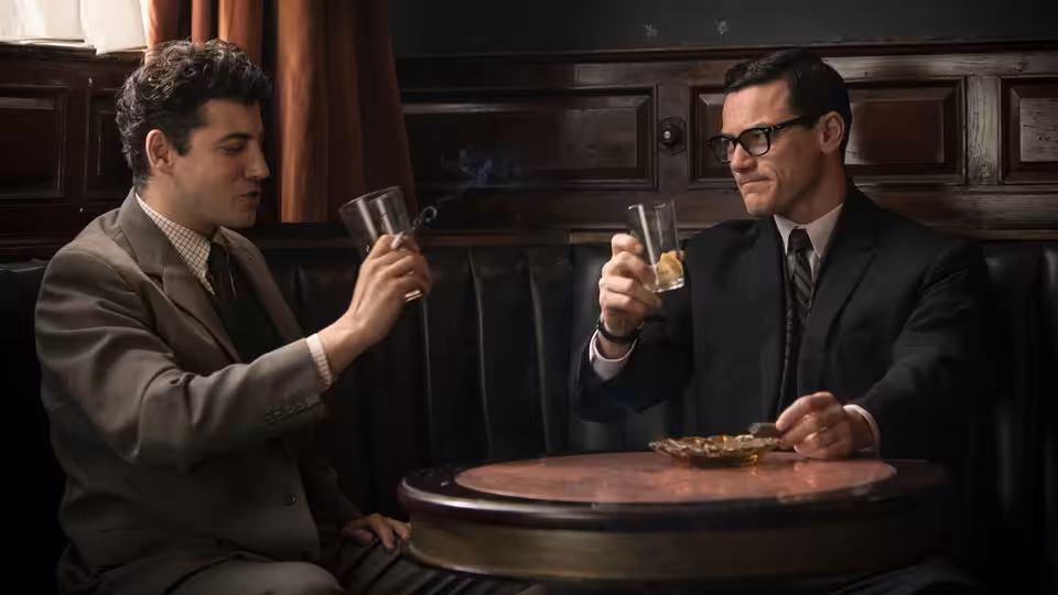 Two men raise their glasses across a small table in a wood-paneled pub