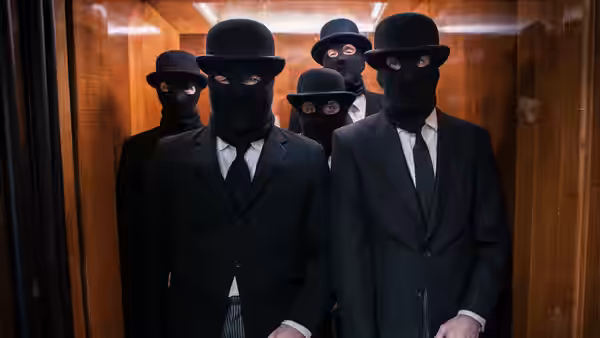 Masked men in suits and bowler hats crowd inside a wooden train carriage