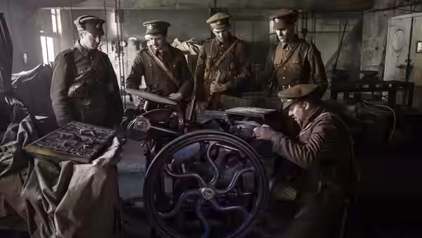 British officers gather around a printing press in a crowded wartime workshop
