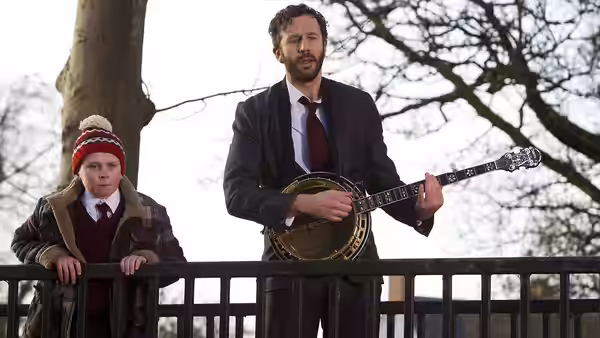 Sean Murphy (Chris O'Dowd) plays a banjo beside Martin Moone (David Rawle) leaning on a railing