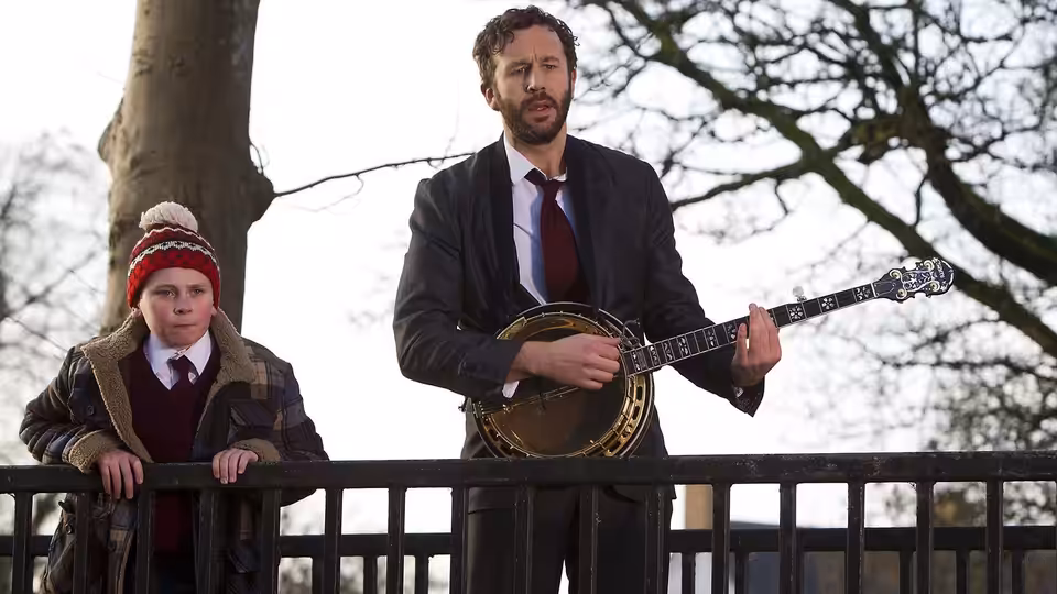 Sean Murphy (Chris O'Dowd) plays a banjo beside Martin Moone (David Rawle) leaning on a railing