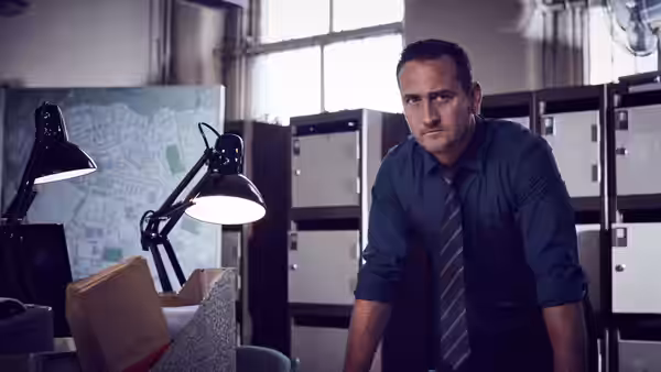 A man in a shirt and tie leans over a desk in a police office