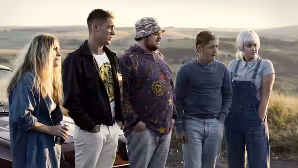 Five people stand beside a car, looking across the countryside