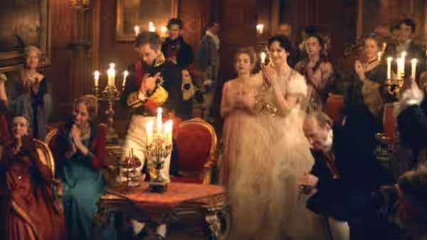 Guests gather around a candlelit table as a uniformed man plays music at a ball