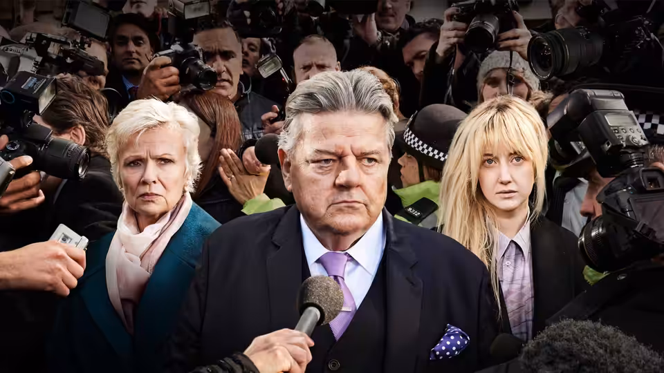 Paul Finchley (Robbie Coltrane) faces reporters with Marie (Julie Walters) and Dee Finchley (Andrea Riseborough) beside him