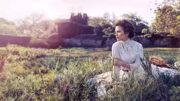Margaret Schlegel (Hayley Atwell) sits in tall grass beside a garden ruin