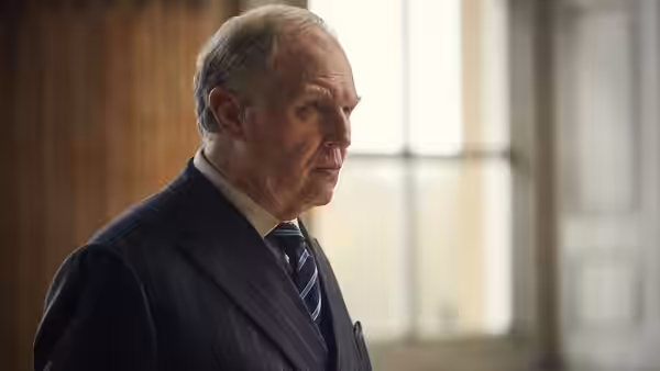 Charles (Tim Pigott-Smith) looks ahead in profile, wearing a pinstriped suit and tie