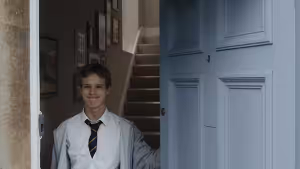 A young man in school uniform smiles from an open doorway