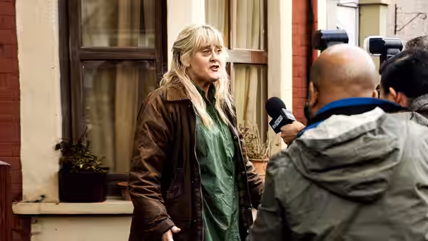 Miriam Grayson (Sarah Lancashire) speaks to reporters outside a house