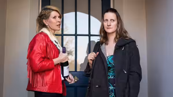 Emma (Julia Davis) holds a bottle beside Sally (Catherine Shepherd) at a doorway
