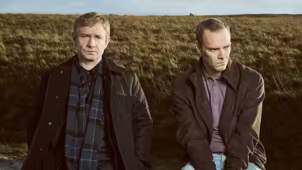 Martin Freeman as Steve Fulcher sits beside a man on a grassy hillside