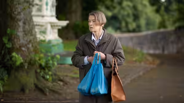 Maud Palmer Horsham (Glenda Jackson) stands on a garden path carrying shopping bags