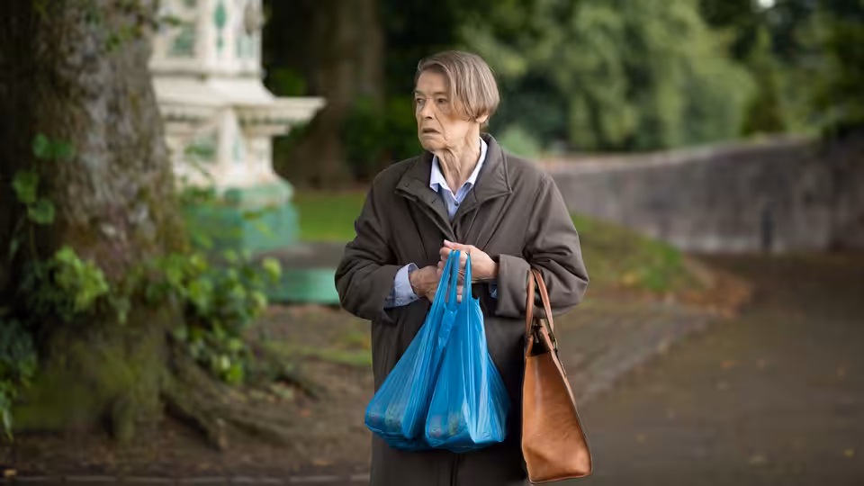 Maud Palmer Horsham (Glenda Jackson) stands on a garden path carrying shopping bags
