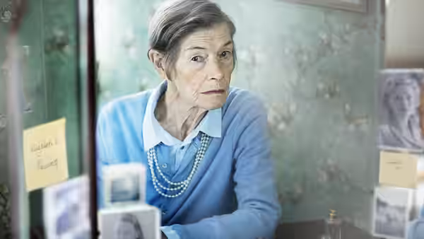 Maud Palmer Horsham (Glenda Jackson) studies photographs and keepsakes behind a glass display