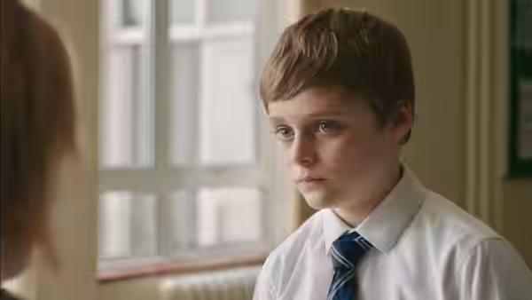 Ray (Billy Barratt), wearing school uniform, looks toward someone across a classroom