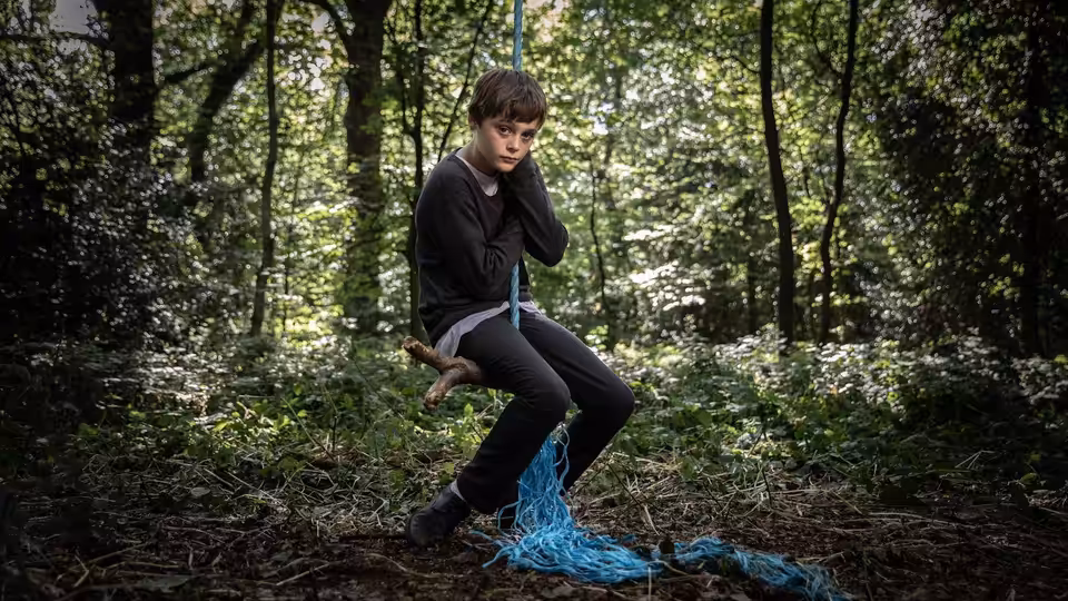 Ray (Billy Barratt) sits on a branch in the woods with a blue rope around him