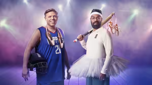 Rob Beckett in a basketball jersey stands beside Romesh Ranganathan in a tutu onstage