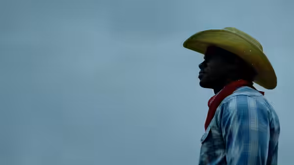 A man in a cowboy hat and red bandana looks across the sky