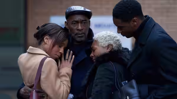 A family huddles together as a woman leans against an older man wearing a cap