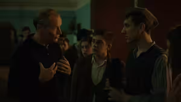 An older man speaks with two young men in a crowded room