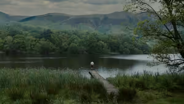 A lone person stands at the end of a wooden jetty on a lake