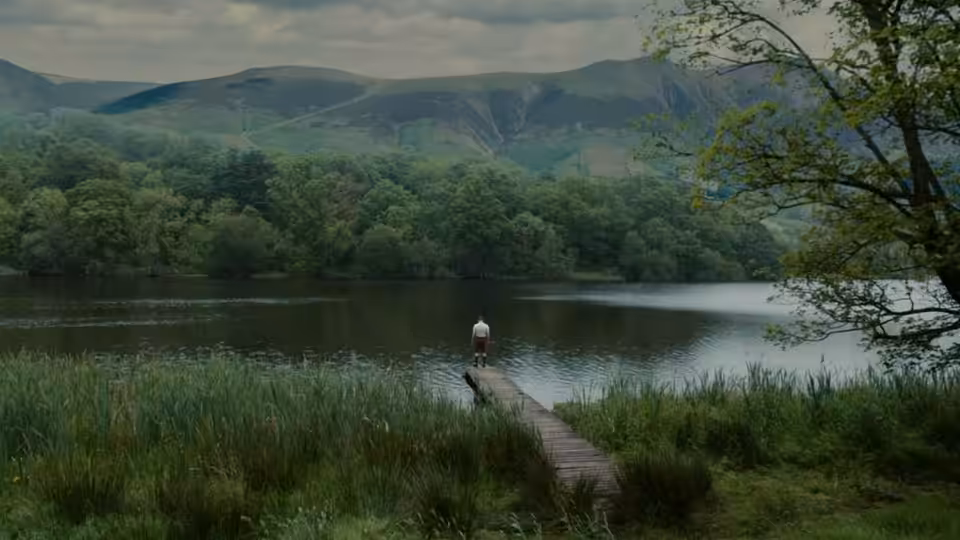 A lone person stands at the end of a wooden jetty on a lake