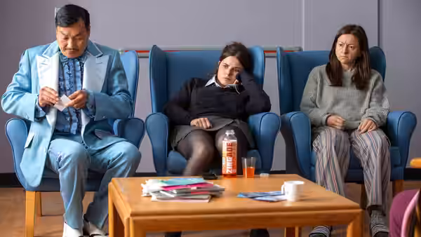 Bethan slouches between two adults in a clinic waiting room